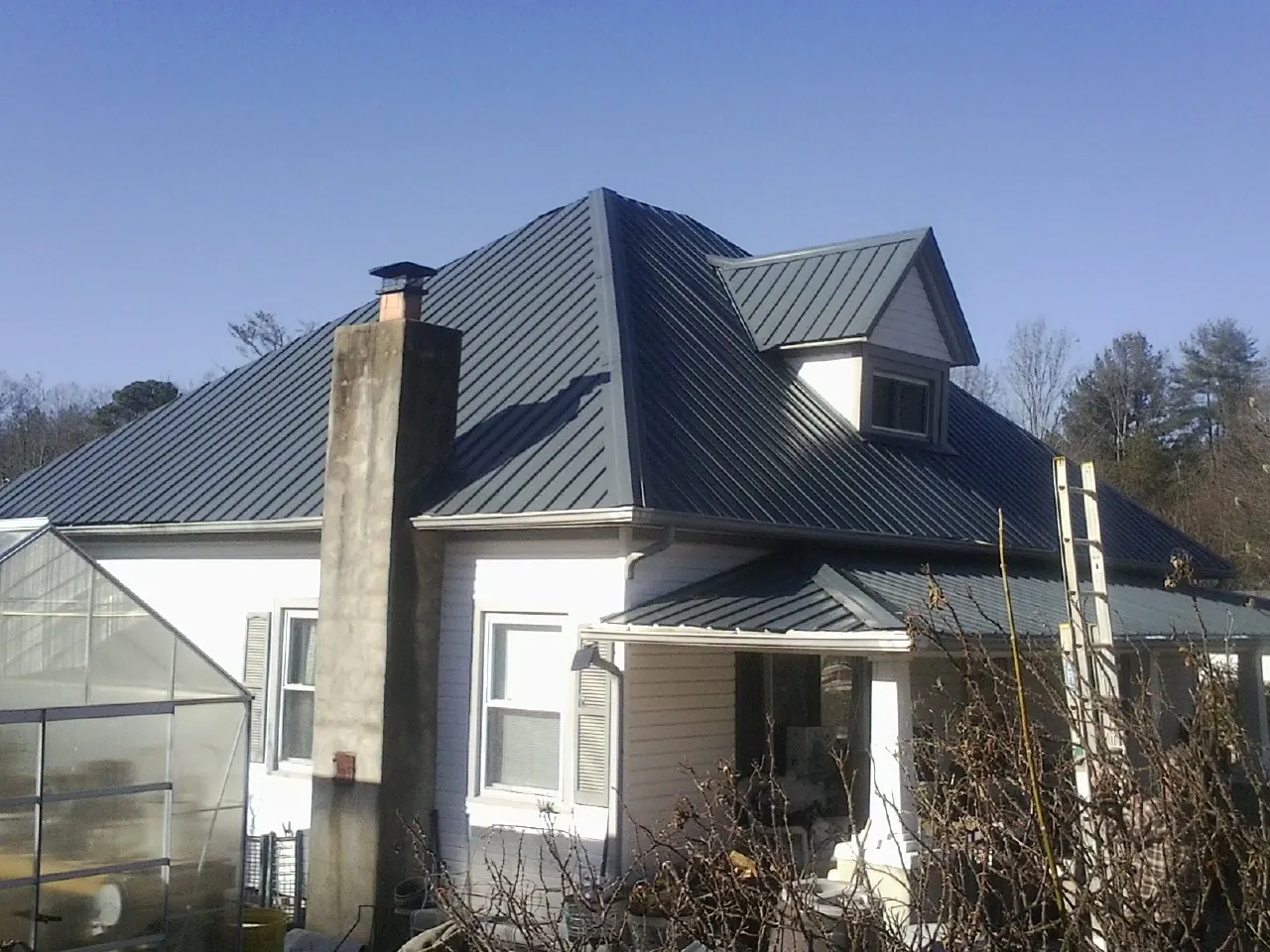 Dark blue standing seam metal roof on a white farmhouse with dormer — Slate & Tile Roof Repair by Roofing Brothers in Jansen