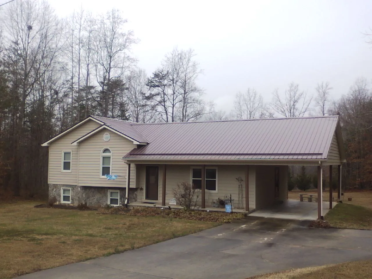 Burgundy metal roof on a tan split level home with an attached carport in Jansen