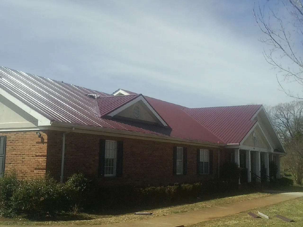Red metal roof with gabled entries on a long brick building, from a Hail Damage Roof Repair job in Jansen