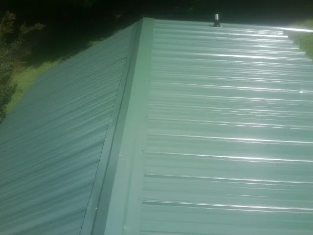 New green metal panels meeting at the ridge of a roof — Flat Roof Repair work by our crew in Jansen