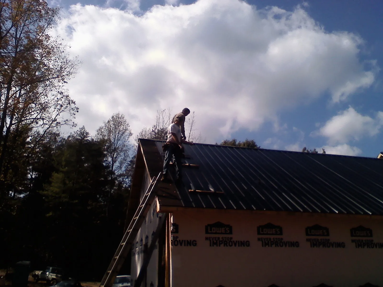 Roofer fastening dark metal panels high against a cloudy sky, from a Roof Inspection job in Jansen
