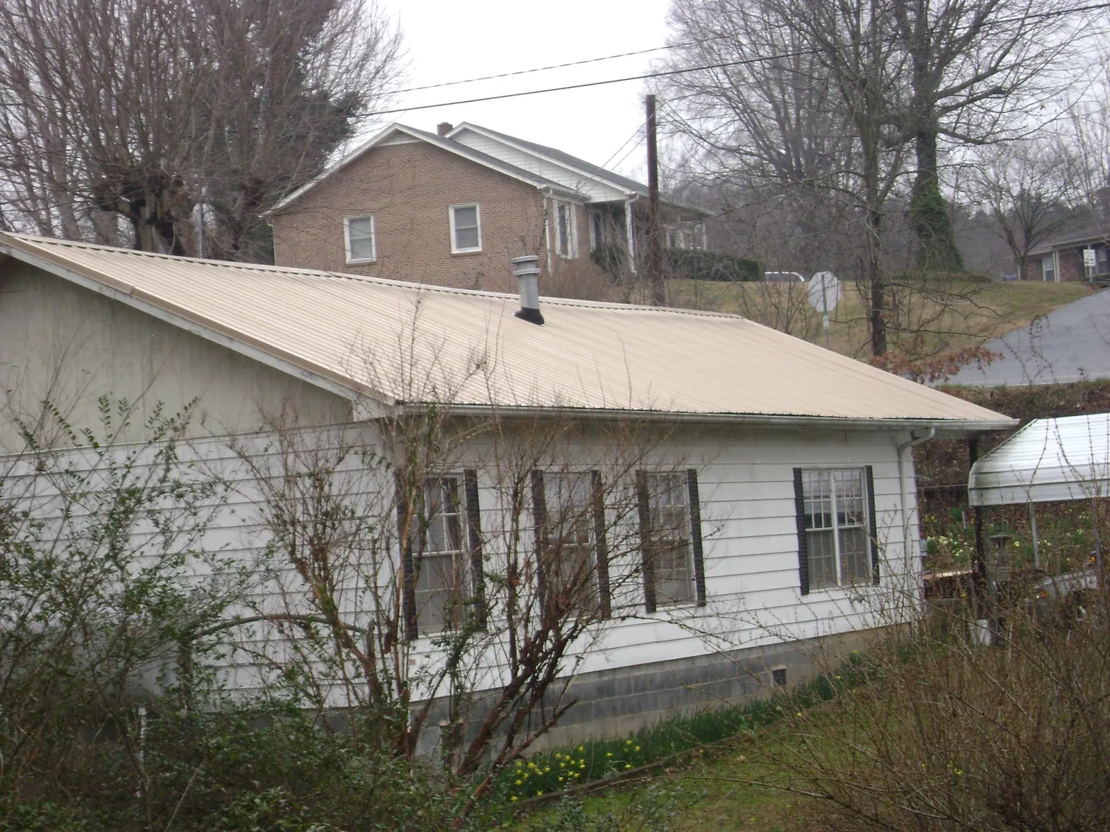 Tan metal roof on a white sided house set into a hillside — Commercial Roofing by Roofing Brothers in Jansen