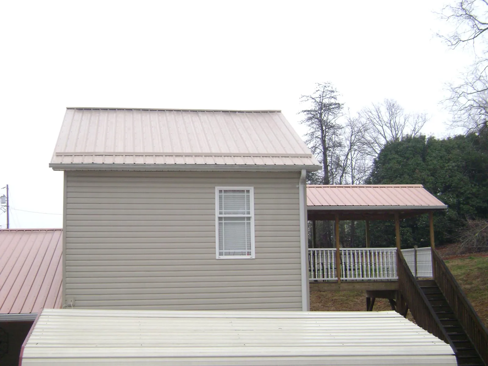 Tan metal roofs on a two story addition and attached porch, from a Roof Replacement job in Jansen